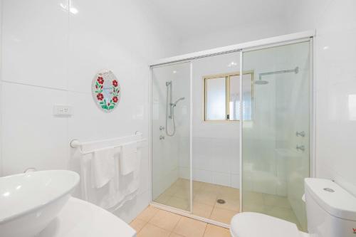 a white bathroom with a shower and a toilet at Sun Catcher - ocean views, walk to beach, lake, cafés, shops in Lake Cathie