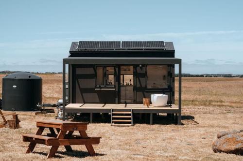 a black tiny house with a table and a bench at Tiny Lenore in Dunkeld