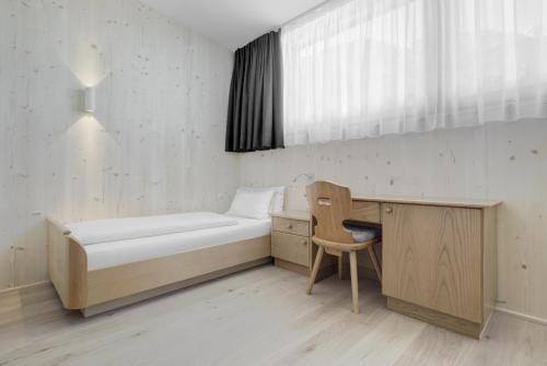 a bedroom with a bed and a desk and a window at Hotel Gardenazza in Badia