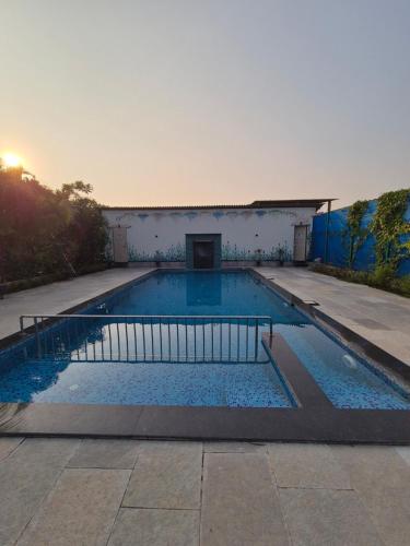 a large swimming pool with the sun setting in the background at Windchime Cottages in Alibaug