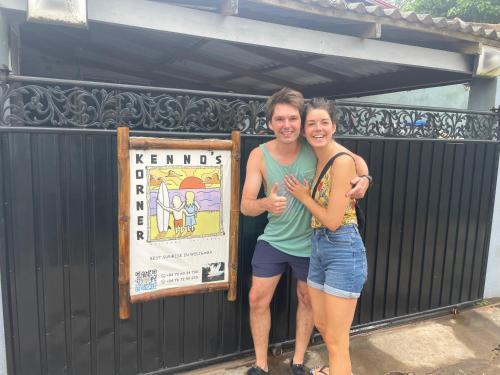 a man and a woman standing in front of a sign at Kenno's Korner in Weligama