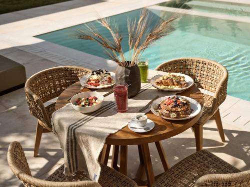 a table with plates of food on it next to a pool at Vorto Luxury Villas, a Signature Island Retreat, By ThinkVilla in Zakynthos