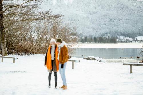 two people standing in the snow next to a lake at Seehotel Berau in St. Wolfgang
