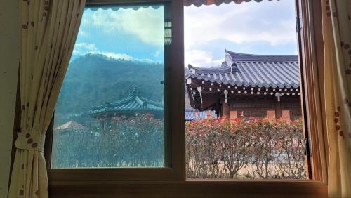 a window with a view of a building and flowers at Boseong Greenery Hanok Pension in Boseong