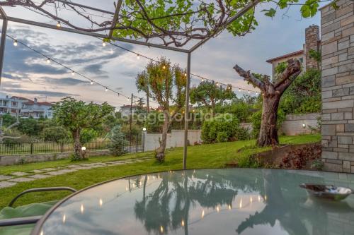 a glass table in a backyard with a tree at Τraditional fully detached villa on a luxurious hillock of Thessaloniki with its own garden also for family & wedding gatherings for 10 to 25 people only 15 minutes from airport in Thessaloniki