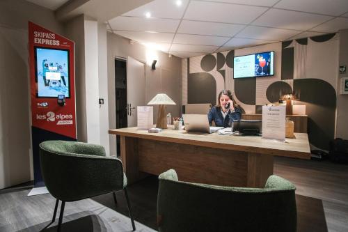 a woman talking on a cell phone at a reception desk at Hôtel Les 2 Alpes L'Orée Des Pistes in Les Deux Alpes