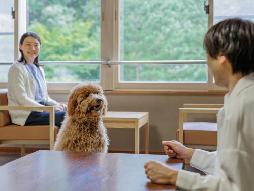 a dog sitting at a table next to a woman at KAMENOI HOTEL SHIOBARA Dog Friendly Hotel in Nasushiobara