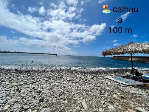 a beach with a straw umbrella and the ocean at Caniçal houses - Madeira in Caniçal