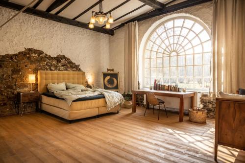 a bedroom with a bed and a desk and a large window at Gut Neuwerk in Kall