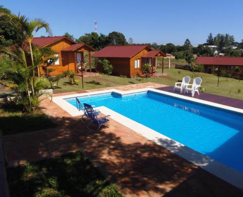 a swimming pool with two chairs and a house at Cabañas Doralia in Oberá