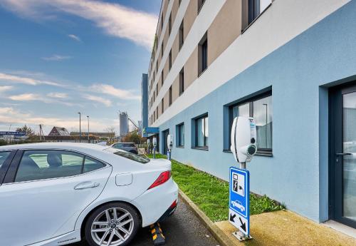 a white car parked next to a building with a parking meter at B&B HOTEL Deauville-Touques in Deauville
