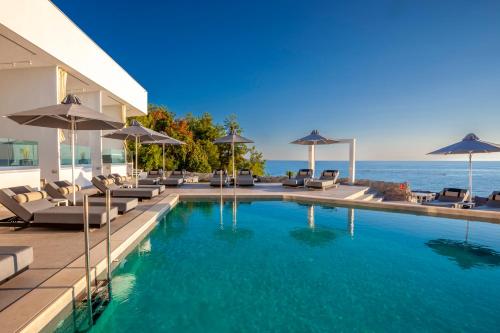 a swimming pool with chairs and umbrellas next to the ocean at Akrotiri Olympus Luxury Suites - Adults Only in Plaka Litochorou