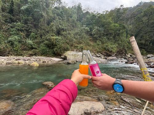 two people holding up drinks in front of a river at Odyssey Stays Rimbi in Pelling