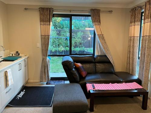 a living room with a leather couch in front of a window at New two Bedroom house attached to main house in Pukekohe East
