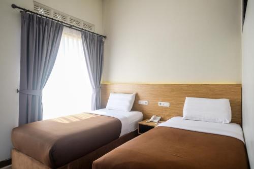 two beds in a hotel room with a window at Amerta Giri Hotel Dieng Wonosobo in Kejajar