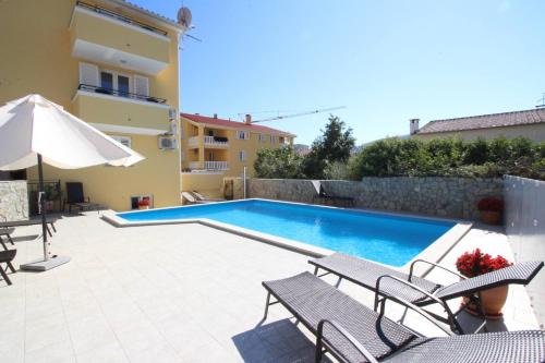 a swimming pool with chairs and an umbrella next to a building at Apartments Gorica 2 in Baška