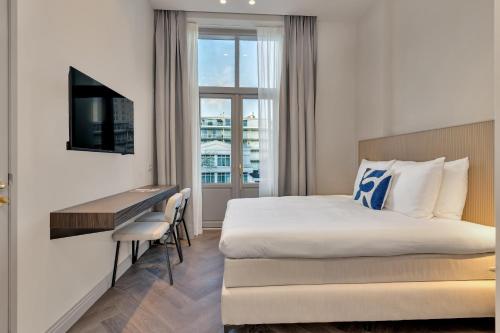a hotel room with a bed and a desk and a television at Hotel Kobalt - Den Haag in The Hague