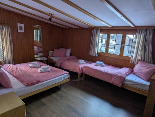 a room with three beds with pink sheets and windows at Hotel Schützen Lauterbrunnen in Lauterbrunnen