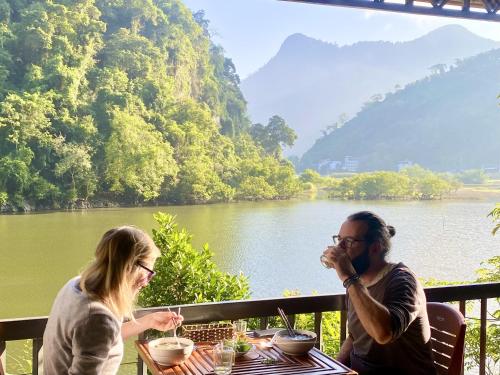 twee personen aan een tafel met uitzicht op een rivier bij Ba Be Lakeside Bungalow in Ba Be18
