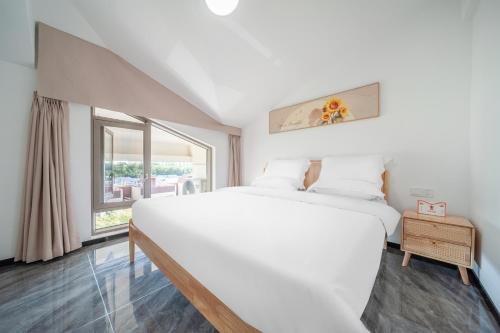 a white bedroom with a large bed and a window at Shiguanghui in Sanya