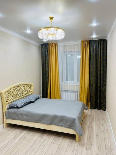 a bedroom with a bed with yellow curtains and a chandelier at Apartments comfort new, Aktau 16 77 in Aktau