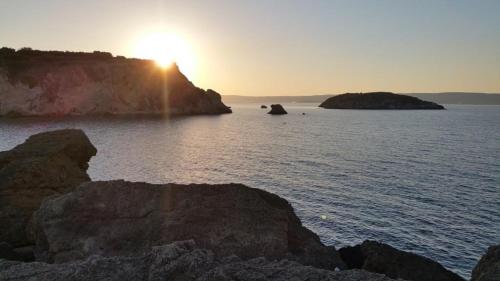 a sunset over a large body of water with rocks at Paradise in Áyios Andhréas