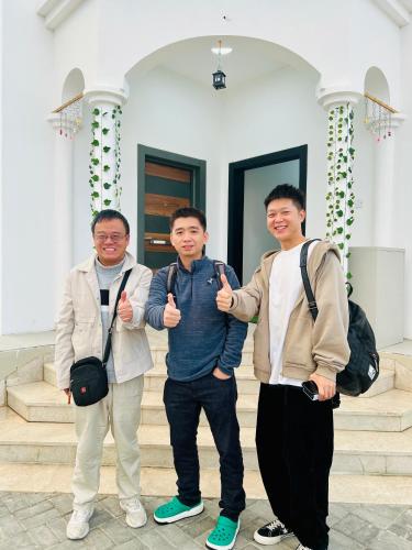 three men giving thumbs up in front of a building at Sukoon Hostel in Muscat