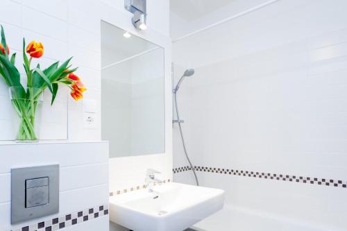 a white bathroom with a sink and a vase of flowers at GreatStay Apartment - Maybachufer in Berlin