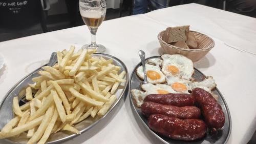 a table with a plate of food with sausage and french fries at Hostal A Cantina de Renche in Renche
