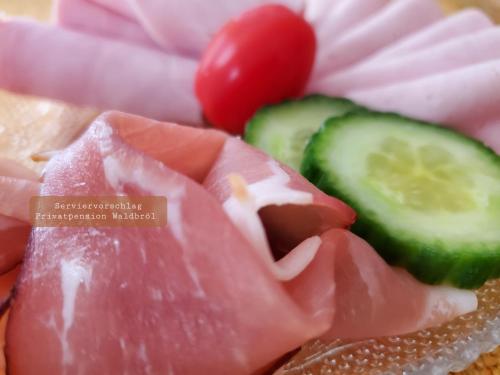 a plate of food with ham cucumbers and a tomato at Privatpension Waldbröl in Waldbröl
