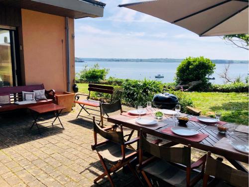 - une table en bois avec des chaises et un parasol sur la terrasse dans l'établissement Rare Grande Villa Incroyable vue mer, à Roscanvel