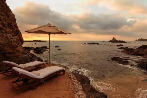 two lounge chairs and an umbrella on the beach at ZOA Hotel - Adults Only in Mazunte
