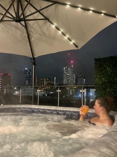 a woman in a bath tub with a glass of juice at Luxury Penthouse with Private Hot Tub Overlooking Leeds City Centre in Leeds