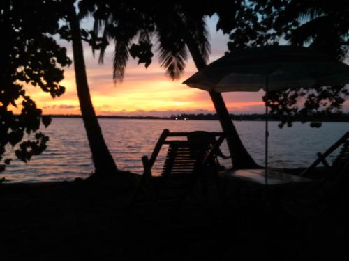 a beach chair and an umbrella on the water at sunset at West Wind Homez - Home Stay in Cochin
