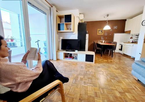 a woman sitting in a chair reading a book in a living room at Apartment San Izola - near the beach in Izola