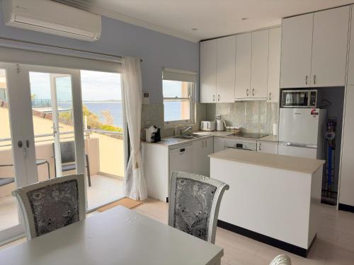 a kitchen with white cabinets and a table and chairs at Sunny Apt on The Esplanade - Aircon in Cronulla