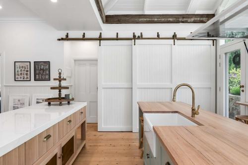 Il comprend une cuisine avec des murs blancs, du parquet et un évier. dans l'établissement SPRIGG COTTAGE Adelaide Hills Luxury Retreat, à Crafers