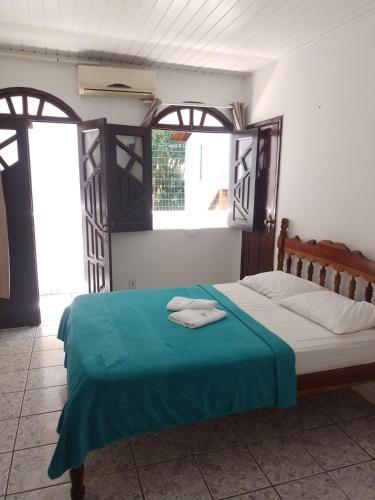 a bedroom with a bed with a blue blanket and two windows at Pousada Sol & Mar in Cayru