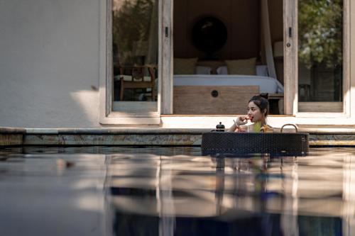 a young girl sitting at a table next to a swimming pool at Kayumanis Sanur Private Villa and Spa in Sanur