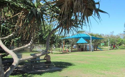 a person sitting on a park bench under a tree at Little Gem in Peregian Beach - walking distance to beach with pool in Peregian Beach