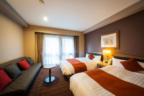 a hotel room with two beds and a couch at Hotel Patio Dogo in Matsuyama