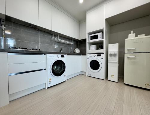una cucina con mobili bianchi, lavatrice e asciugatrice di Eunhasu D&M Residence a Daejeon
