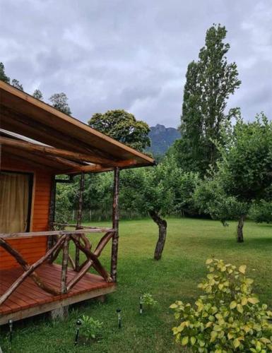 a wooden cabin with a green field and trees at Cabañas GAROVE in Panguipulli
