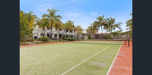 a tennis court in front of a house with palm trees at Noosa Sound - 2brm Townhouse in Noosaville