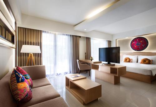 a hotel room with a bed and a couch and a television at Sense Sunset Hotel Seminyak in Seminyak