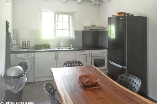 a kitchen with a wooden table and a black refrigerator at Appartement charmant à Sainte-Rose avec terrasse et jardin – 65 m² in Sainte-Rose