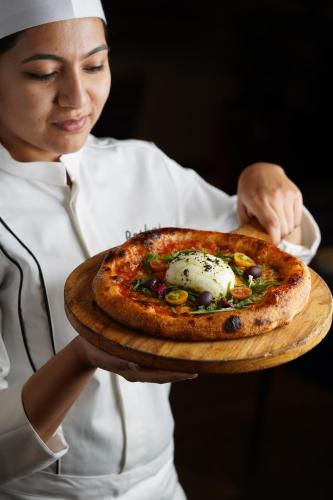 a woman holding a pizza on a wooden plate at Courtyard by Marriott Bhopal in Bhopal