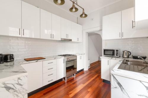 a white kitchen with wooden floors and white cabinets at Quaint 3-Bed Heritage Home in the Heart of Sydney in Sydney