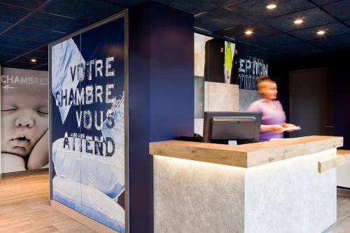 a woman standing behind a counter with a computer at ibis budget Saint-Omer Centre in Saint-Omer