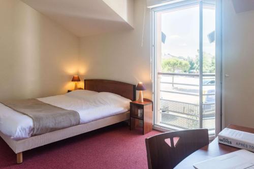 a bedroom with a bed and a view of a balcony at Comfort Aparthotel Nantes La Beaujoire in Nantes
